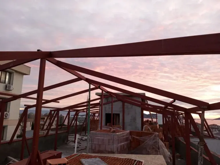 Gün batımında bir apartman çatısında kırmızı astarlı demir çatı makasları