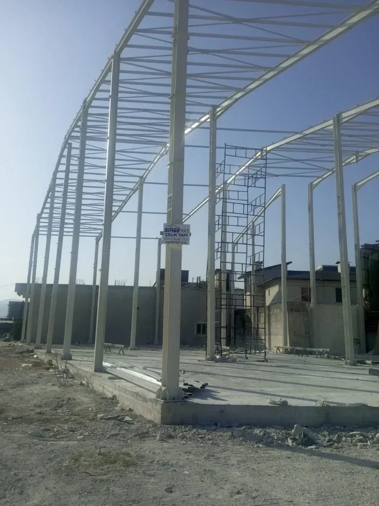Beton zemin üstünde yükselen açık renkli çelik kolonlar ve çatı makasları