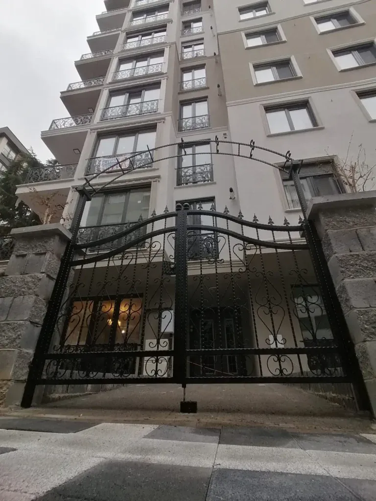 Yüksek bir apartmanın girişinde kemerli, süslemeli çift kanatlı ferforje kapı