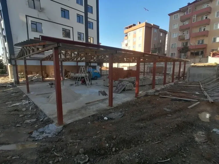Apartmanlar arasındaki arsada kırmızı astarlı demir kolonlu sundurma iskeleti