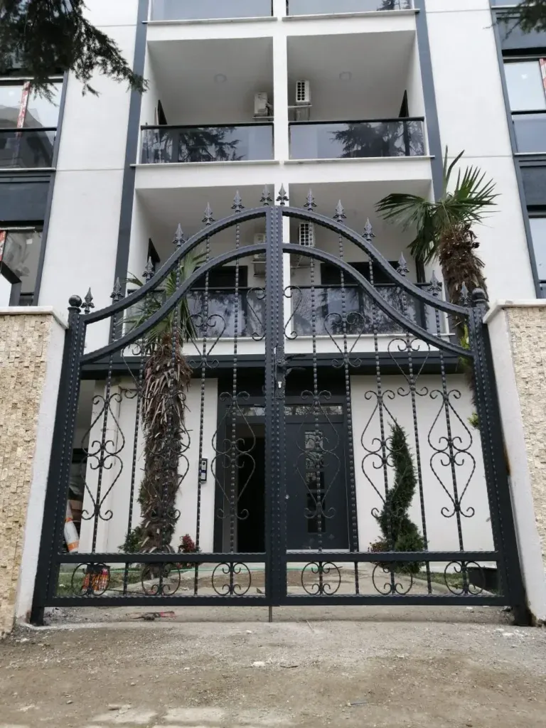Beyaz cepheli bir apartmanın girişinde mızrak uçlu, süslemeli ferforje kapı