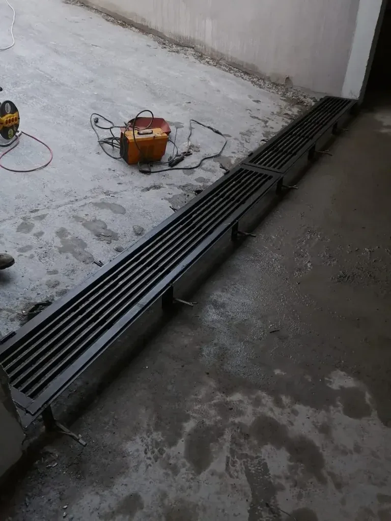 Terasta duvar dibine yerleştirilen siyah ızgaralı metal kanal ve kaynak makinesi